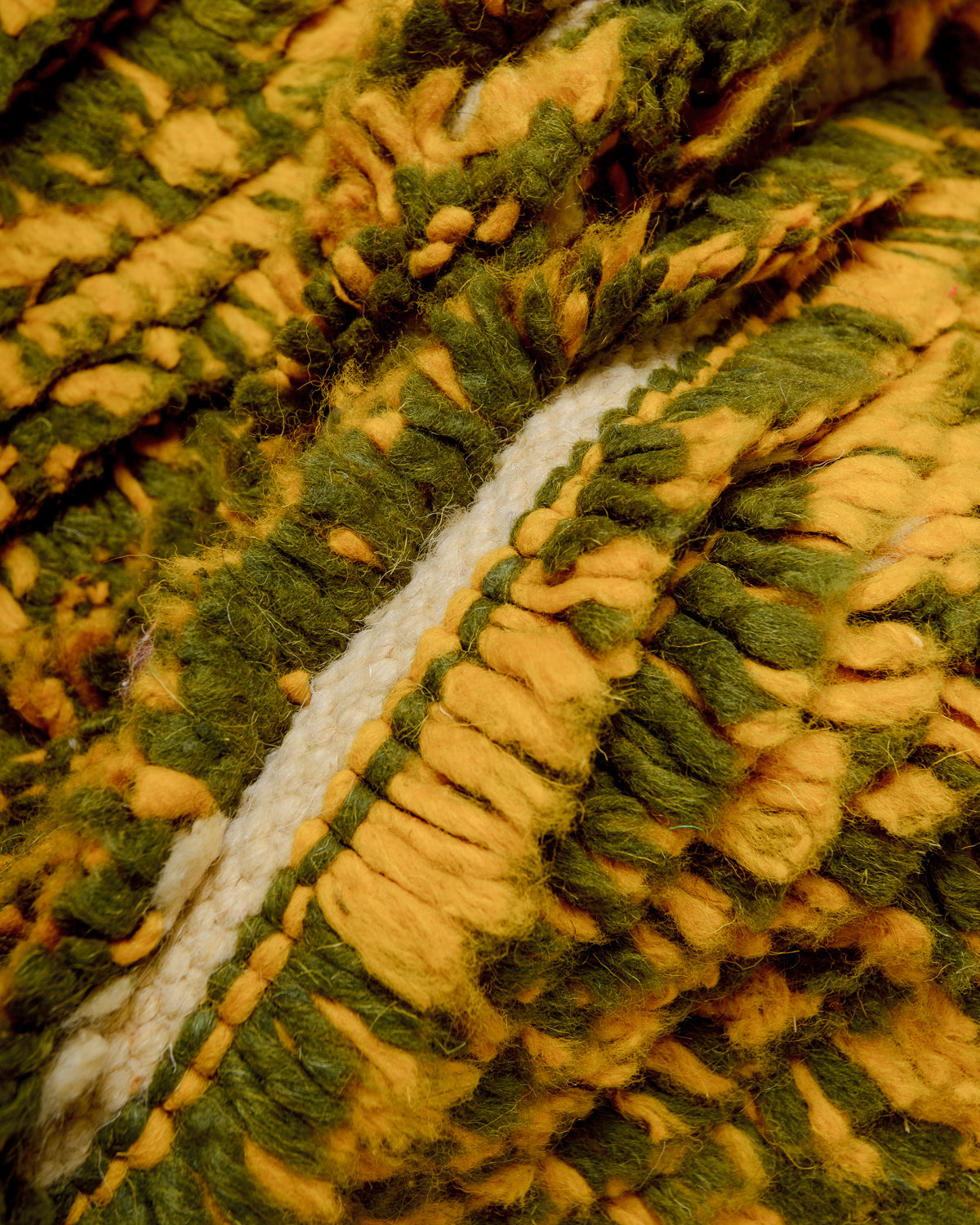 Texture of rug made of knotted yellow and olive wool and flat woven cream wool.